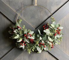 a christmas wreath hanging on the side of a wooden door with greenery and berries