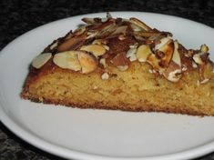 a piece of cake with nuts on top sits on a white plate, ready to be eaten