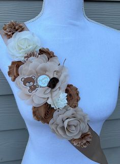 a woman wearing a brown and white flower sash with teddy bear on the front, in front of a gray background