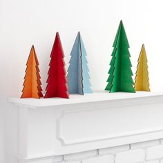 three colorful christmas trees sitting on top of a mantle