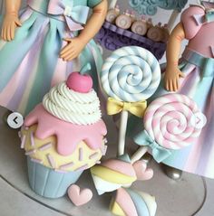 two dolls standing next to some cupcakes and lollipops