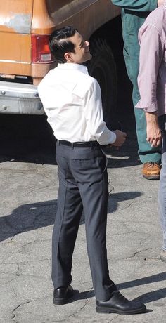 a man standing in front of a yellow bus talking to another man who is wearing a white shirt and black pants