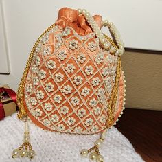 👛 Our beautiful orange potli bag with beadwork is the ideal adornment for any special occasion. The potli bag is made of high-quality raw silk fabric and embellished with intricate beadwork in a lovely pastel orange color. The drawstring closure on the Indian bag is lined with soft satin. It is the ideal size for carrying your essentials like your phone, wallet, and keys. 👛 This orange potli bag is ideal for weddings, parties, and other formal occasions. It can also be dressed down for a more Intricate Embroidered Evening Potli Bag For Festivals, Formal Bollywood Embroidered Potli Bag, Festive Bohemian Embroidered Potli Bag, Wedding Potli Bag With Intricate Embroidery, Traditional Evening Potli Bag With Intricate Embroidery, Potli Purse, Embroidered Clutch Purse, Satin Purses, Red Bangles