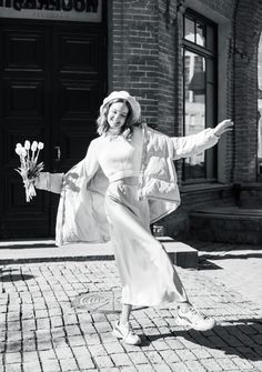 black and white photograph of woman in front of brick building with flowers on the sidewalk