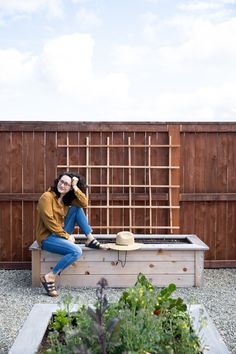 a woman sitting on top of a wooden bench next to a planter filled with flowers