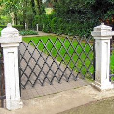 an iron gate is in the middle of a sidewalk and grassy area with trees behind it