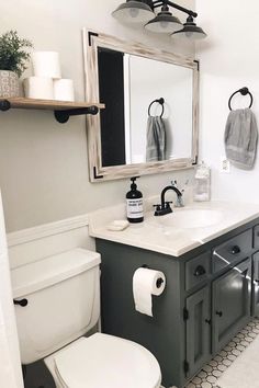 a white toilet sitting next to a sink in a bathroom under a mirror and towel rack