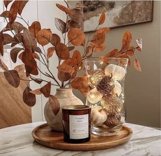 a candle sits on a table next to a vase filled with leaves and acorns