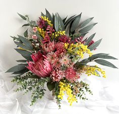 a vase filled with lots of flowers and greenery on top of a white sheet