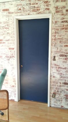 an empty chair in front of a brick wall with a blue door on the other side