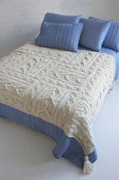 a white bed with blue pillows and blankets on it's headboard, next to a brick wall