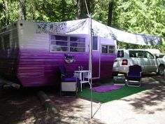 a purple and white trailer parked in the woods next to a car with a tent on it