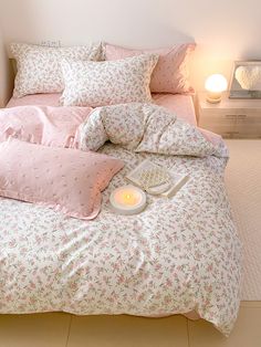 a bed with pink and white floral comforter on it, next to a lit candle