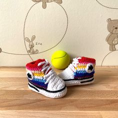 a crocheted tennis shoe next to a yellow ball on a wooden surface with teddy bears in the background