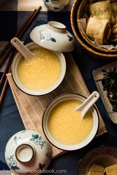 two bowls filled with soup sitting on top of a table next to plates and chopsticks