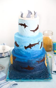 a three tiered cake decorated with blue and white frosting, topped with shark fin decorations