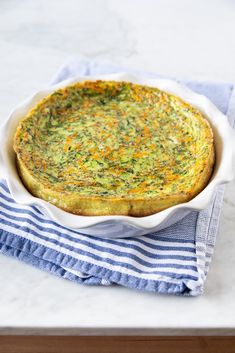 a quiche in a white dish on a blue and white towel