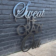 a metal sign that reads sweat the crazy one on it's side next to a brick wall