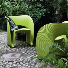 two green chairs sitting next to each other on a cobblestone walkway in front of trees and bushes