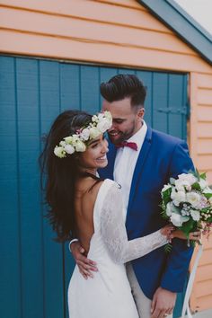 a bride and groom standing in front of a blue garage door holding their bouquets