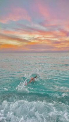 a person swimming in the ocean under a colorful sky at sunset or sunrise with clouds