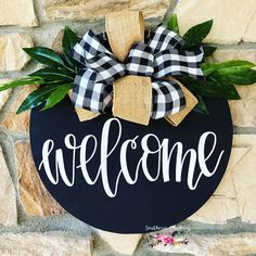 a welcome sign is hanging on a stone wall with greenery and burlocks