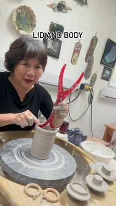 a woman is making a vase out of clay on a spinning wheel with red scissors