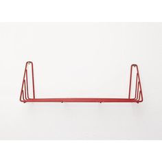 a red metal shelf on the wall with two hooks hanging from it's sides