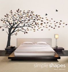 a bed sitting under a tree next to a wall mounted with birds flying over it