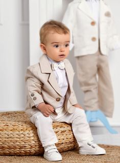 a little boy in a suit and bow tie sitting on a wicker basket next to a mannequin