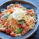 pasta with tomatoes, mozzarella and herbs in a bowl on a wooden table