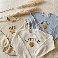 three sweaters with smiley faces on them and the words big little written in black