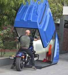 a man sitting on a motorcycle in front of a blue tent that looks like a car