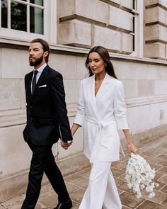 a man and woman dressed in white walking down the street holding hands with each other