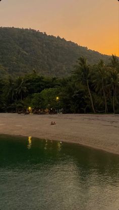 the sun is setting at the beach with palm trees and mountains in the back ground