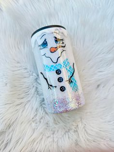 a white can with a snowman painted on it sitting on top of a furry surface