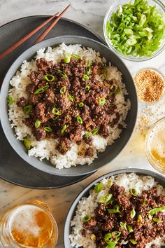 two bowls filled with meat and rice next to chopsticks on a marble table