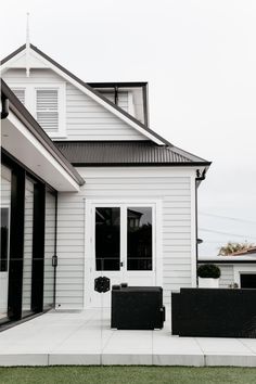 a white house with black furniture in front of it and grass on the side yard