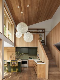 an open kitchen and dining area with wood flooring, white pendant lights hanging from the ceiling