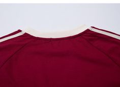 the back of a maroon shirt with white trims on it, against a gray background