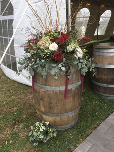 a wooden barrel with flowers and greenery in it sitting on the grass next to two wine barrels