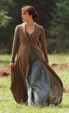 a woman is walking in the grass wearing a long dress and brown cardigan coat