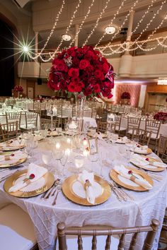 the table is set with white and gold plates, silverware, red flowers and candles