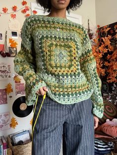 a woman standing in front of a wall holding a record and wearing a crocheted sweater