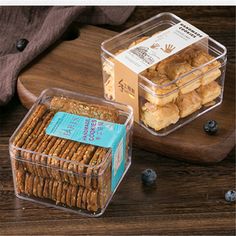 two plastic containers filled with crackers on top of a wooden cutting board next to blueberries