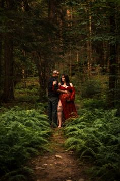 a man and woman standing in the middle of a forest with ferns on the ground