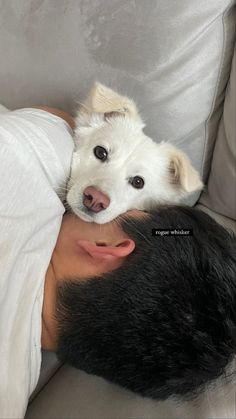 a man laying on top of a white couch next to a dog in his lap