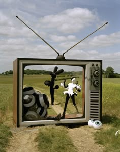 an old tv sitting in the middle of a field with two people dancing on it