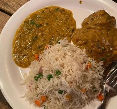 a white plate topped with rice and meat covered in gravy on top of a wooden table