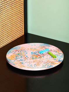 a black table with a colorful plate on it and a green wall in the background